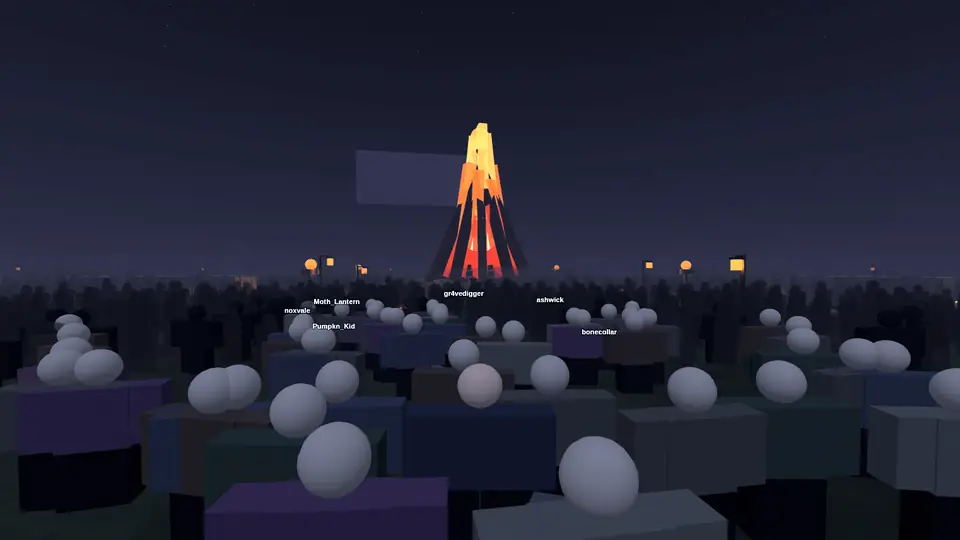 A crowd gathered on a dark field around a towering bonfire